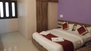 A bedroom with a bed, a wooden wardrobe, a window with blinds, and an air conditioning unit. - Hotel Always Welcome (Abu Road)