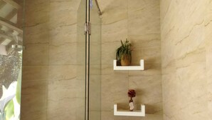 A glass-enclosed shower area with a marble wall, a potted plant, and a small vase on a shelf. - Villa Kania Parangtritis (Sewon)