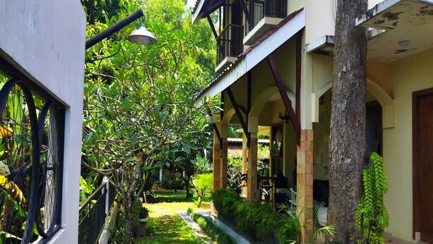 A courtyard with a pathway, surrounded by greenery and a building with a balcony. - Villa Kania Parangtritis (Sewon)