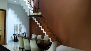 A dining area with a wooden staircase and a white wall. - Villa Kania Parangtritis (Sewon)