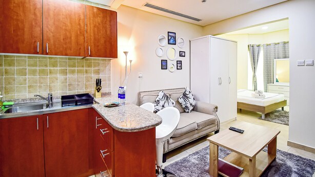 A compact hotel room with a kitchenette, a sofa, a bedside table, and a bathroom visible through an open door. - DNL AMAZING DEAL Cozy studio in JLT (Dubai)