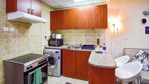 A compact kitchen with a stove, microwave, and washing machine. - DNL AMAZING DEAL Cozy studio in JLT (Dubai)