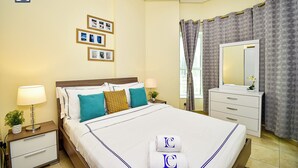 A hotel room with a neatly made bed, a bedside table with a lamp, a dresser with a mirror, and a wall with framed pictures. - DNL AMAZING DEAL Cozy studio in JLT (Dubai)
