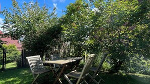 An outdoor seating area with a wooden table and chairs, surrounded by lush greenery and a clear blue sky. - Cozy Scandinavian-style vacation home between the Schlei and the Baltic Sea (Rieseby)