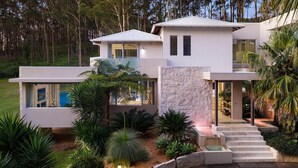 A modern two-story house with a stone facade, large windows, and a landscaped garden. - Colenso Luxury Home, Perfect for Friends & Family (Erina)