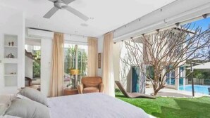 A modern bedroom with a large bed, a ceiling fan, and a view of a swimming pool and garden. - Colenso Luxury Home, Perfect for Friends & Family (Erina)