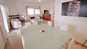 Moderni olohuone, jossa on lasinen ruokapöytä, valkoiset sohvat ja takka.