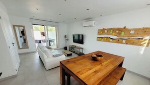 Een moderne woonkamer met een houten eettafel, een witte bank en een aan de muur bevestigde televisie.