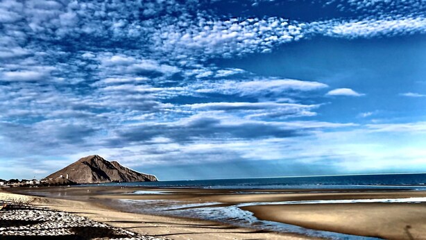 En strand med et bjerg i baggrunden og en klar himmel.