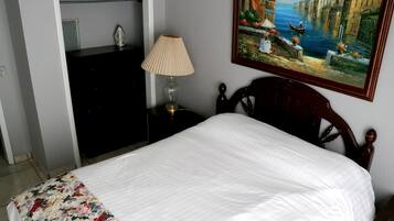 A neatly made bed with a floral bedspread, a bedside lamp, and a painting of a canal scene on the wall.
