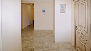 Un couloir doté d’un sol en marbre, une porte ornée de moulures décoratives et un tableau encadré accroché au mur.