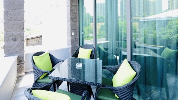Un balcon doté de meubles en osier et d’une table en verre, offrant une vue sur le paysage urbain.