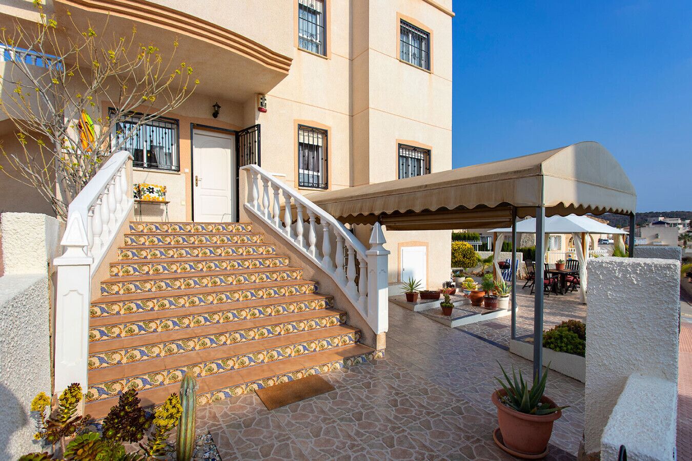 L’entrée d’un hôtel, avec un escalier carrelé, un espace extérieur aménagé avec des sièges et des plantes en pot.