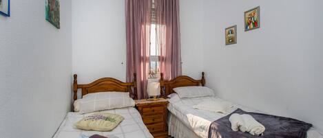 Een slaapkamer met twee eenpersoonsbedden, een houten hoofdbord, een nachtkastje, een raam met gordijnen en wanddecoratie.