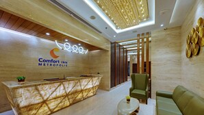 A hotel reception area with a reception desk, a green sofa, and a modern chandelier.