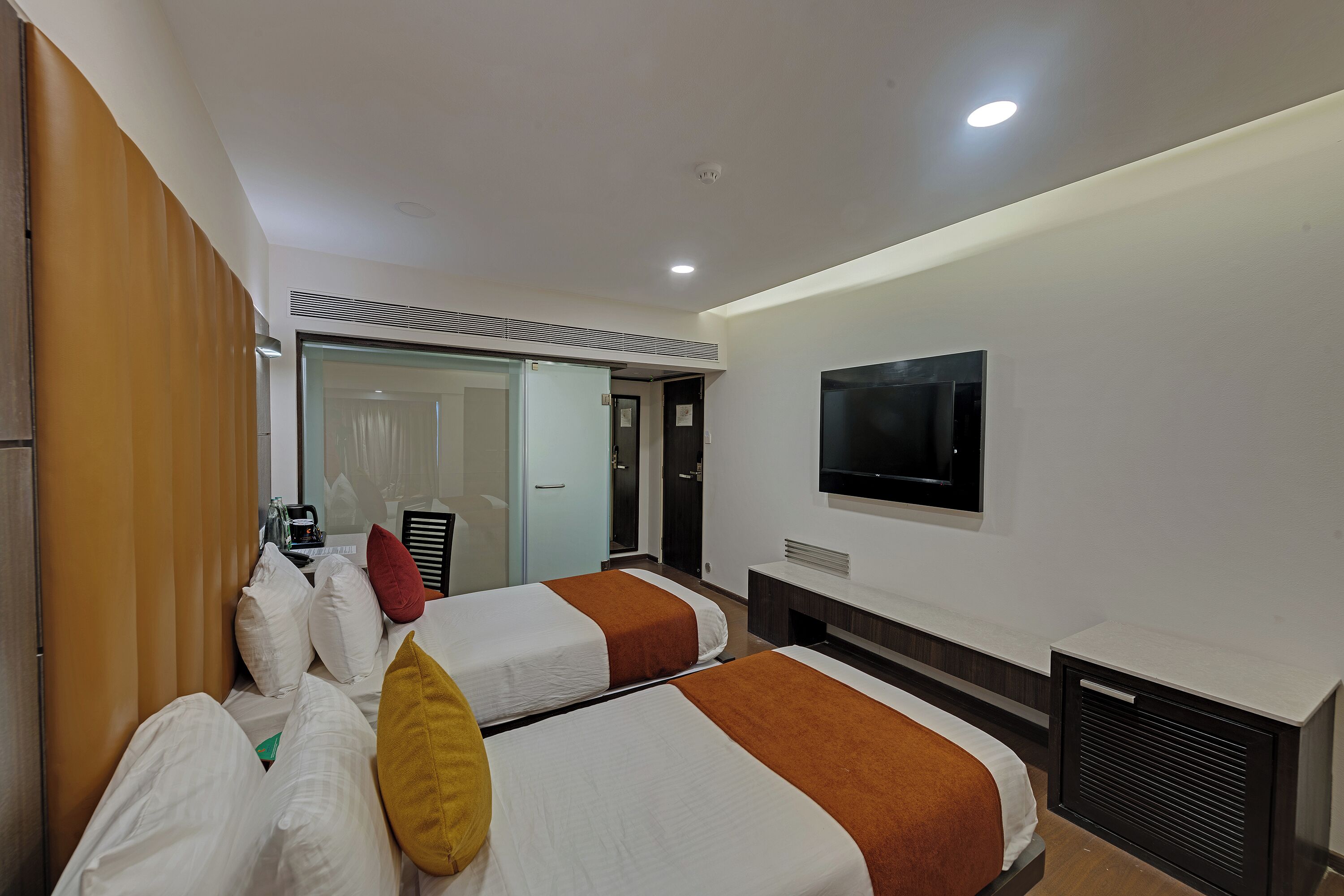 Habitación de hotel con dos camas, televisión y puerta corredera que da a un baño.