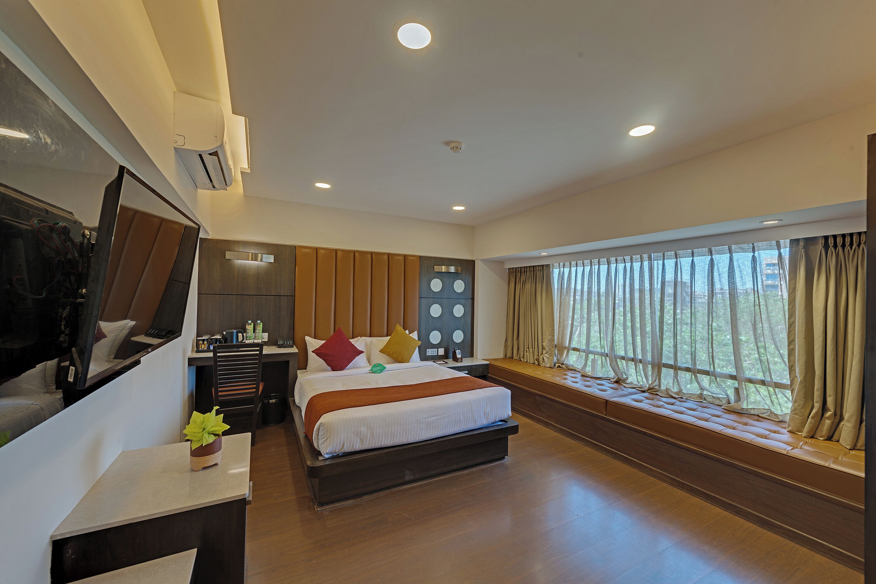A modern hotel room with a large bed, a desk, a TV, and a window with curtains.