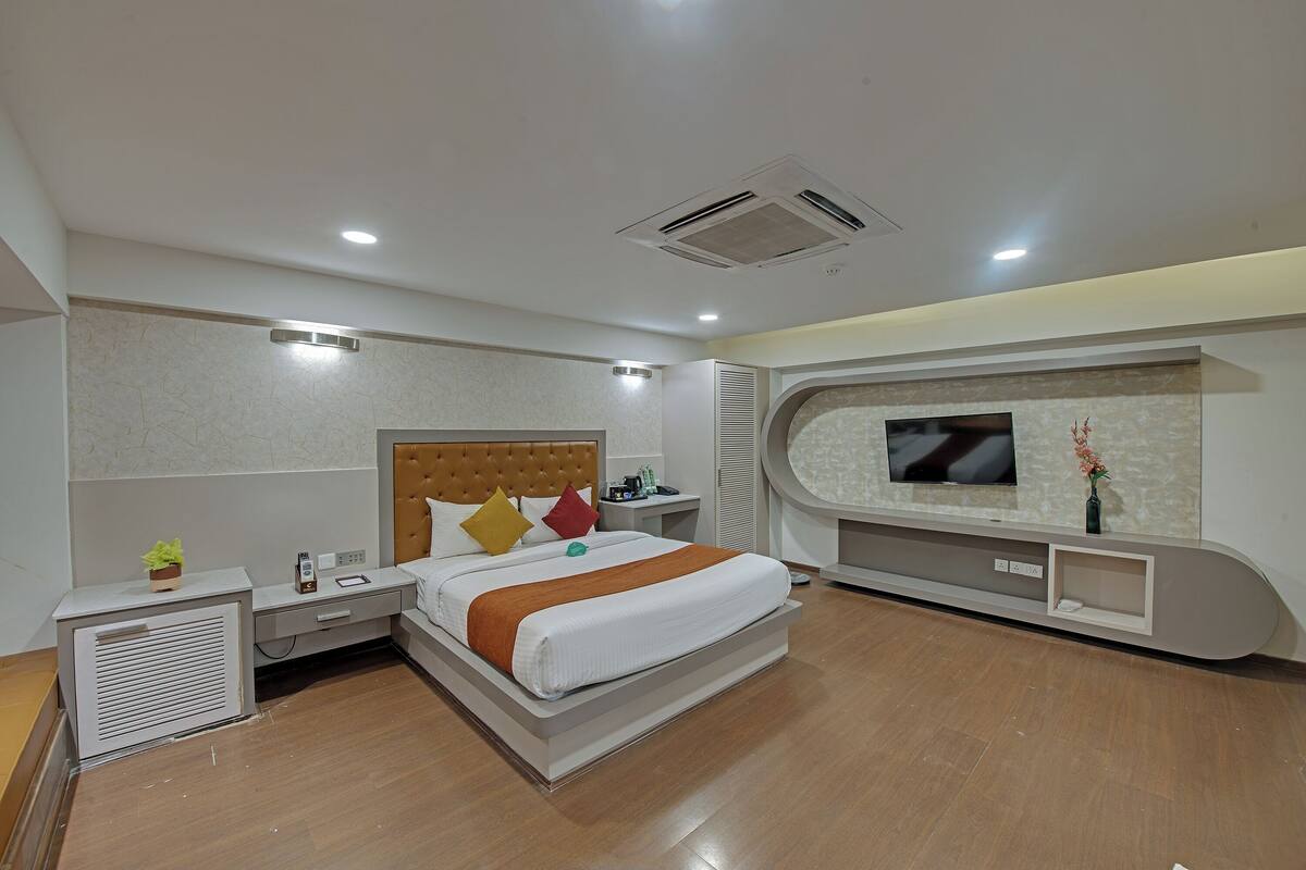 Moderni hotellihuone, jossa on suuri sänky, seinälle asennettu televisio, yöpöytä ja sisäänrakennettu säilytystila.