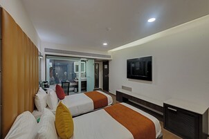 Habitación de hotel con dos camas, televisión, escritorio y baño visible a través de una puerta abierta.