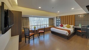 A modern hotel room with a large bed, a desk, a chair, a TV, and a window with curtains.