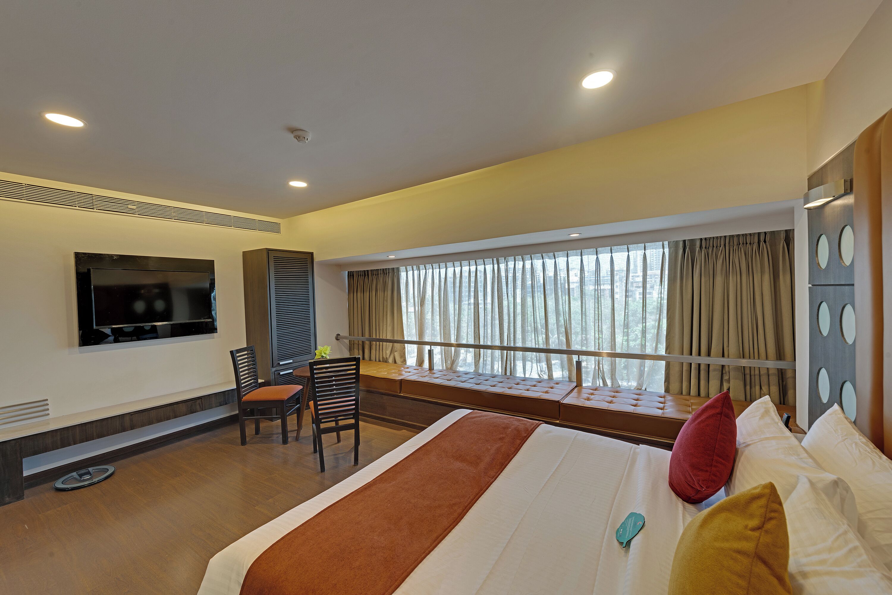 A hotel room with a bed, a TV, a desk, and a window with curtains.