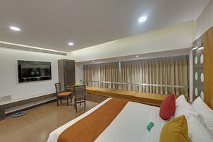 A hotel room with a bed, a TV, a seating area with a view, and a window with curtains.