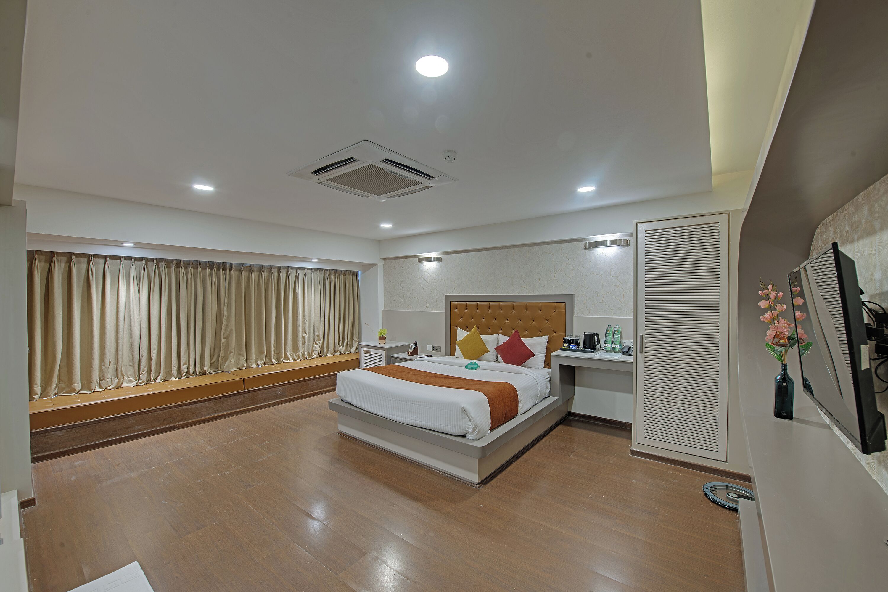 A modern hotel room with a large bed, a bedside table, a nightstand, a window with curtains, and a wall-mounted TV.