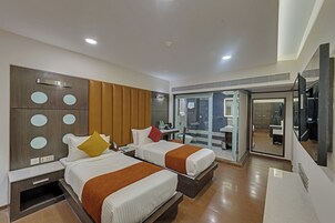 A hotel room with two beds, a desk, a mirror, and a bathroom visible through a glass door.