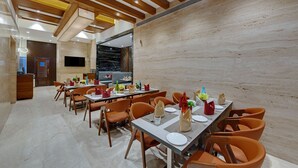 A dining area with wooden ceiling beams, marble walls, and a flat-screen TV mounted on the wall.