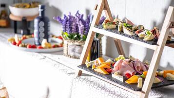A cheese board with various types of cheese and accompaniments, a bottle of olive oil, and a bowl of fruit on a table.