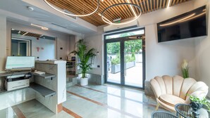 A modern reception area with a flat-screen TV, a reception desk, a potted plant, and a comfortable seating area with a chair and a small table. - Campeador Inn (Cluj-Napoca)