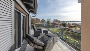 Un balcon doté de meubles en osier et offrant une vue sur un lac et des maisons.