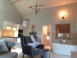 Un salon moderne avec un grand fauteuil, un canapé et une vue sur la cuisine et la salle de bain.