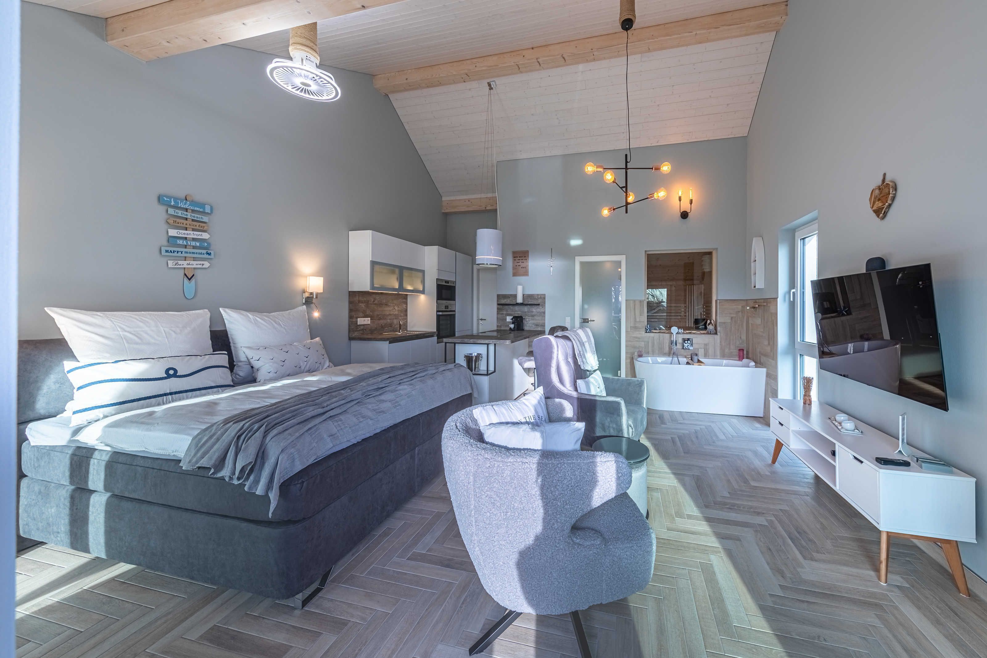Un dormitorio moderno con una cama grande, una silla, un televisor y un baño a la vista.