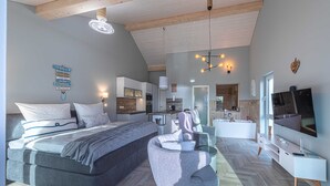Une chambre à coucher moderne avec un grand lit, une chaise, un téléviseur et une salle de bain visible au fond.