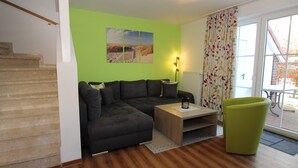 Una sala de estar con un sofá modular, una mesita de centro de madera, un sillón verde y un cuadro en la pared.