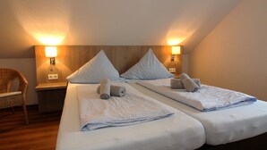 Habitación de hotel con dos camas, cada una con una almohada y una toalla enrollada. Hay lámparas de pared a cada lado de las camas.