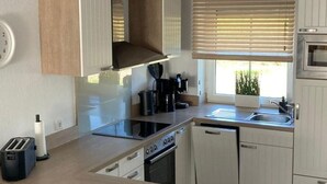 Une cuisine moderne dotée d’un îlot central, d’un four encastré et d’une fenêtre avec stores.