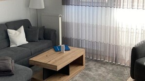 Un salon moderne avec un canapé gris, une table basse en bois, un lampadaire et des rideaux légers.