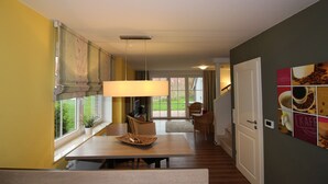 A dining area with a table, chairs, a lamp, and a view of the outdoors through large windows. - ROB 06 for 6 persons, approx. 78 sqm - Feriendorf Robbenplatte Burhave (1) (Butjadingen)
