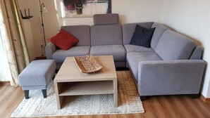 A modern living room with a grey sectional sofa, a wooden coffee table, and a red pillow. - ROB 06 for 6 persons, approx. 78 sqm - Feriendorf Robbenplatte Burhave (1) (Butjadingen)