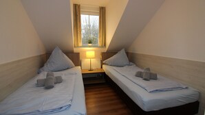 A small, cozy room with two single beds, a nightstand with a lamp, and a window with curtains. - ROB 06 for 6 persons, approx. 78 sqm - Feriendorf Robbenplatte Burhave (1) (Butjadingen)