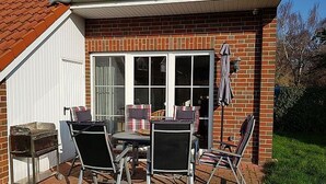 A patio with a brick house, a grill, and a table with chairs. - ROB 06 for 6 persons, approx. 78 sqm - Feriendorf Robbenplatte Burhave (1) (Butjadingen)