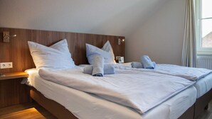 A hotel room with a wooden headboard, a large bed with white linens, and a window with curtains. - ROB 07 for 6 persons, approx. 78 sqm - Feriendorf Robbenplatte Burhave (1) (Butjadingen)
