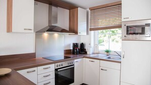 A modern kitchen with white cabinets, a wooden countertop, a built-in oven, a microwave, and a window with blinds. - ROB 07 for 6 persons, approx. 78 sqm - Feriendorf Robbenplatte Burhave (1) (Butjadingen)
