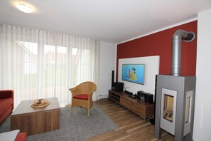 Uma sala de estar com lareira, televisão, sofá vermelho, mesa de centro de madeira e uma poltrona de vime.