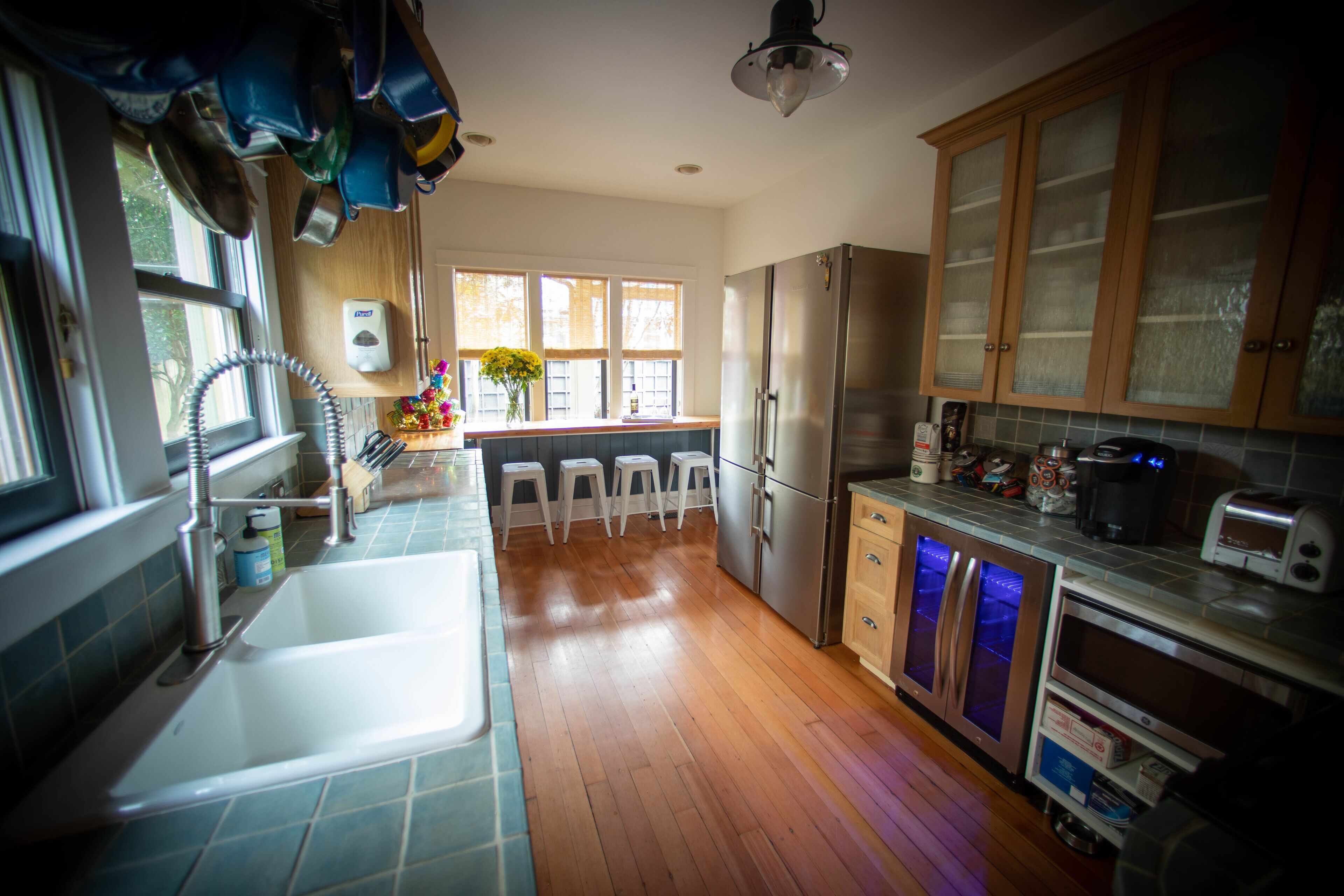 A kitchen with wooden cabinets, a stainless steel refrigerator, a sink, and a window with a view of trees.