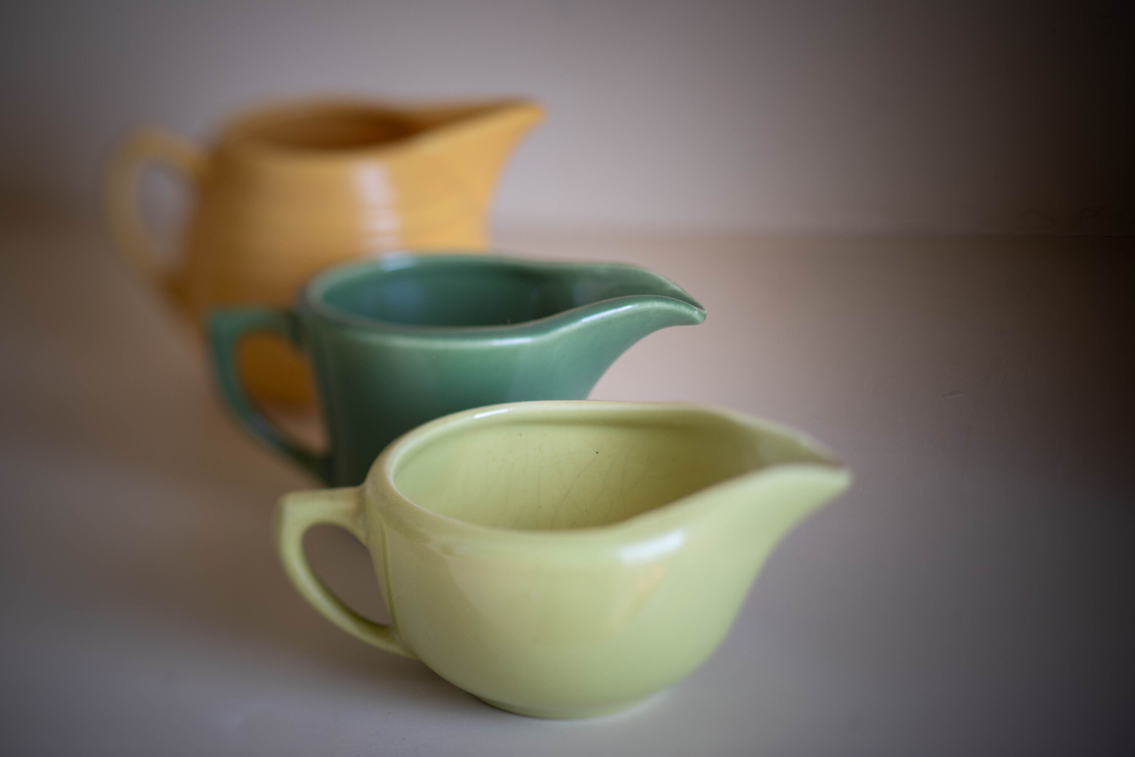 Three ceramic pitchers of different colors on a flat surface.