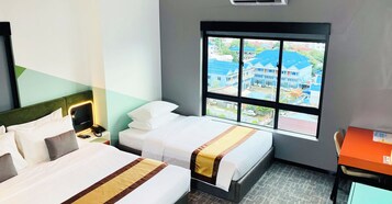 A hotel room with two beds, a desk, and a window with a view of buildings.