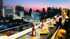 Un comedor con vistas a la ciudad, una mesa con comida, bebidas y una persona sentada.